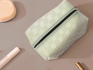 Compact green cosmetic bag with zipper, placed among makeup items on a flat surface.